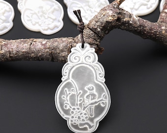 May include: White pendant with a bird and floral design, hanging from a brown cord. The pendant is carved with a bird perched on a branch with flowers. Other similar pendants are visible in the background, along with a brown branch.
