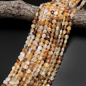 May include: A strand of faceted, translucent, light brown and clear gemstone beads. The beads are oval shaped and have a smooth, polished finish.