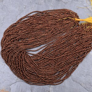 May include: A strand of copper-colored faceted gemstone beads. The beads are small and round, and they have a metallic sheen.