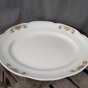 May include: Oval, white ceramic serving platter with a scalloped edge. The rim is decorated with a gold trim and floral patterns in shades of red, green, and gold. A vintage piece.