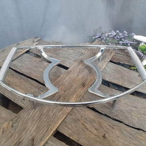 May include: A chrome-plated serving dish warmer with a rectangular frame and curved supports. The handles have a ribbed design. The warmer is designed to hold a dish and keep food warm. The background is a wooden surface.