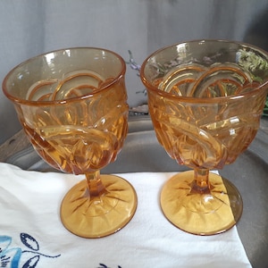 May include: Two amber glass goblets with a swirl design. The goblets have a short stem and a wide bowl.