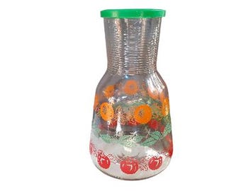 May include: A clear glass pitcher with a green lid and a floral design featuring red and orange fruit. The pitcher has a textured surface.