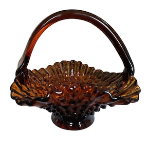 May include: A vintage amber glass basket with a handle. The basket features a textured, hobnail design and a scalloped rim. The handle arches gracefully above the basket, creating a decorative and functional piece.