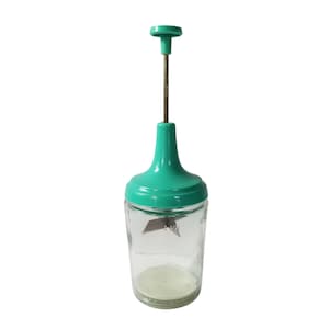 May include: A vintage manual food chopper with a clear glass jar and a teal green plastic top and handle. The chopper has a metal blade inside the jar and a brown metal rod extending to the top.