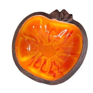 May include: Orange and brown ceramic bowl shaped like an apple. The bowl has a glossy orange glaze with a swirl pattern.