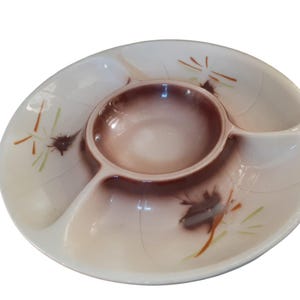 May include: Oval-shaped, divided serving dish with a central dip bowl. The dish is off-white with a brown and tan gradient in the center and brown floral accents. The dish has three sections for serving.