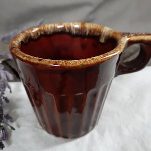 May include: A vintage brown ceramic mug with a ribbed exterior and a distinctive handle. The rim has a contrasting tan and brown glaze. This mug is suitable for coffee, tea, or other beverages.