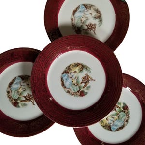 May include: Set of five vintage porcelain plates. Each plate features a white center with a pastoral scene and a textured, burgundy rim with gold accents. The plates are arranged in a slightly overlapping pattern.