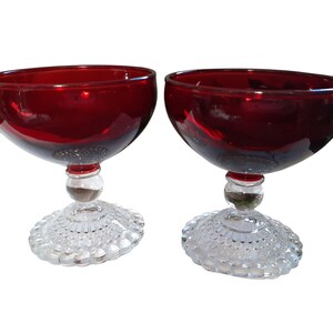 May include: Two red glass dessert bowls with clear, textured bases. The bowls are round and have a wide rim.
