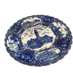 May include: A vintage blue and white decorative plate featuring illustrations of Toronto landmarks. The plate has a scalloped edge and floral accents, with text that reads "Views of Toronto Canada" and "City Hall".