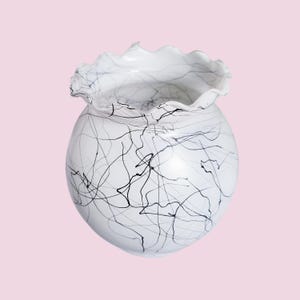 May include: White ceramic vase with a ruffled rim and black swirling lines.