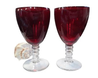 May include: Two red wine glasses with clear stems and a twisted design. The glasses are empty and have a deep red color.