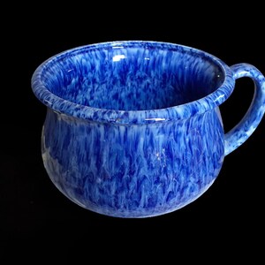 May include: A blue ceramic chamber pot with a white marbled glaze. The pot has a rounded body and a single handle.
