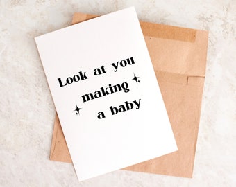 May include: A white card with the text "Look at you making a baby" with two small stars on either side of the word "making". The card is sitting on a brown envelope.