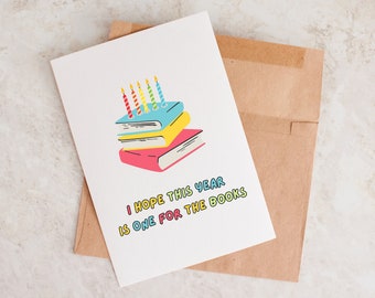 May include: A white card with a colourful illustration of a stack of books with candles on top. The text on the card reads "I hope this year is one for the books."
