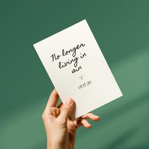 Könnte beinhalten: Eine cremefarbene Karte, die in einer Hand gehalten wird, mit den Worten "No longer living in sin" in schwarzer Schrift geschrieben. Unter dem Text befindet sich ein kleines Herz und das Datum "07.17.26". Der Hintergrund ist ein einfarbiges Teal-Grün.