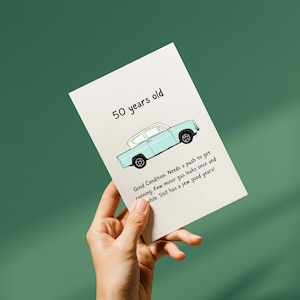 May include: A greeting card held by a hand, with the text "50 years old" and a light blue cartoon car. The card reads: "Good Condition. Needs a push to get running. Few minor gas leaks once and while. Still has a few good years!"