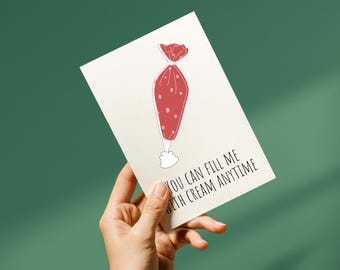 May include: A greeting card held by a hand, featuring a red pastry bag illustration with white polka dots. The text "YOU CAN FILL ME WITH CREAM ANYTIME" is printed in black below the illustration. The background is a solid teal color.