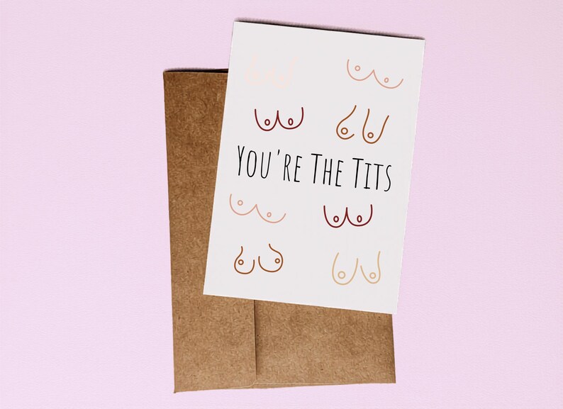 Puede incluir: Una tarjeta de felicitaci&oacute;n con la frase "You're the Tits" en texto negro, acompa&ntilde;ada de ilustraciones de senos en varios colores. La tarjeta est&aacute; colocada sobre un sobre marr&oacute;n sobre un fondo rosa.
