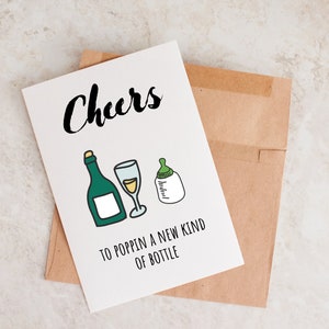 Pode incluir: Um cart&atilde;o branco com texto preto que diz "Cheers to poppin' a new kind of bottle". O cart&atilde;o tem um desenho de uma garrafa de vinho, um copo de vinho e uma mamadeira.