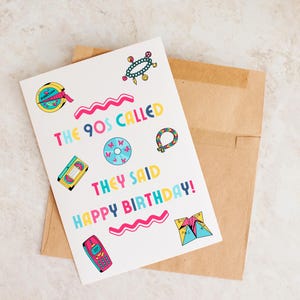 May include: A white birthday card with the text "THE 90S CALLED THEY SAID HAPPY BIRTHDAY!" in colorful bubble letters. The card features 90s-themed graphics like a cassette tape, CD, and a flip phone. The card is on a brown envelope.