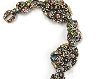 May include: An antique gold-toned bracelet with floral and leaf designs. The bracelet features blue, pink, and green gemstones. The bracelet is made of metal and has a clasp closure. The bracelet is a jewelry item.