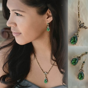 Op de afbeelding: Een vintage-stijl sieradenset met een ketting en oorbellen. De set bevat een ketting met een druppelvormige groene edelsteen hanger en bijpassende oorbellen. Het metaal heeft een goudkleurige tint en de edelstenen zijn heldergroen.