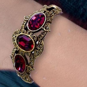 May include: A gold-toned bracelet with a delicate filigree design and four large, oval-shaped, deep red gemstones.