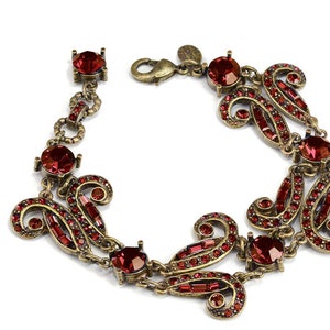 May include: A red crystal and gold tone bracelet with a decorative design. The bracelet has a clasp closure.