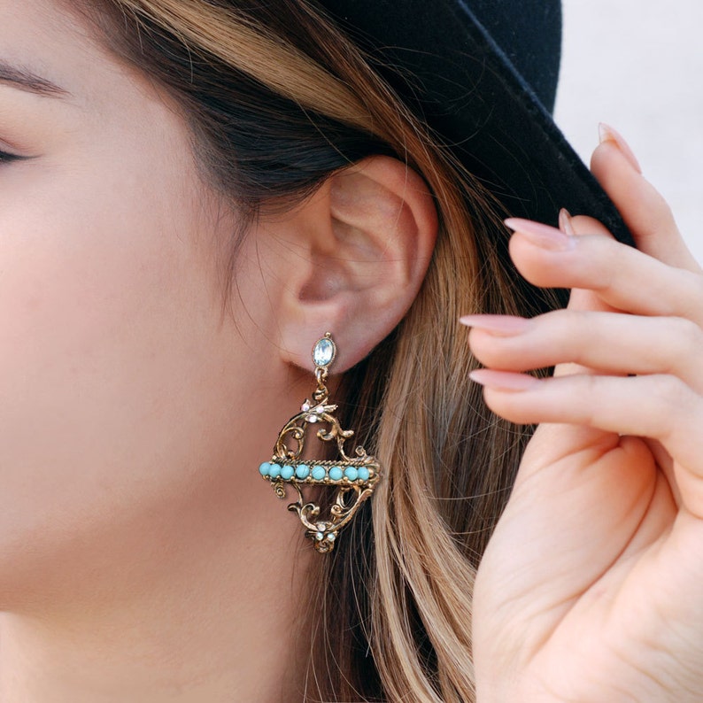 May include: A pair of gold earrings with a turquoise stone design. The earrings feature a delicate, intricate pattern and a single turquoise stone at the top.