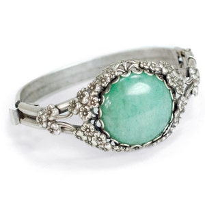 May include: A silver bracelet with a large, round, green gemstone set in a floral design.