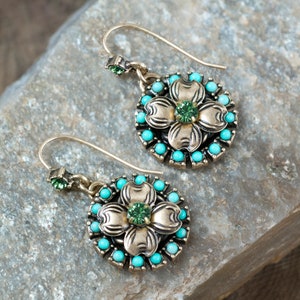 May include: A pair of gold tone earrings with a turquoise and green flower design. The earrings have a drop style with a small green crystal in the center of the flower.