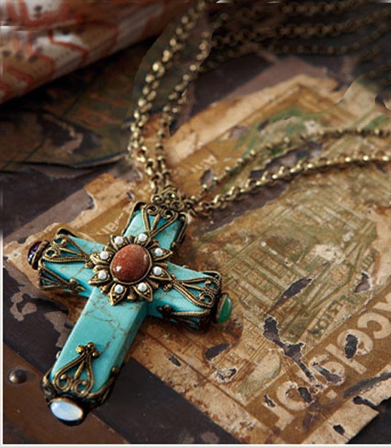 May include: A turquoise cross pendant necklace with ornate gold-toned metalwork and a variety of gemstone accents. The necklace is on a chain with a vintage look.