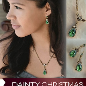 May include: A delicate gold necklace and matching earrings with teardrop-shaped green gemstones. The necklace features a pendant with a small cluster of crystals. The earrings are dangle style with a small crystal accent.