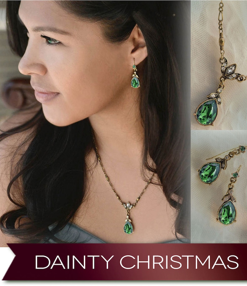 May include: A delicate gold necklace and matching earrings with teardrop-shaped green gemstones. The necklace features a pendant with a small cluster of crystals. The earrings are dangle style with a small crystal accent.