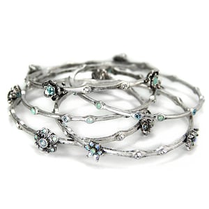 May include: Set of five silver-toned bangle bracelets with delicate floral accents and light blue gemstones.