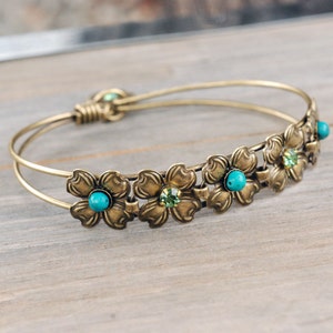 May include: A gold-toned bangle bracelet with a double wire design. The bracelet is adorned with five flower-shaped charms, each with a turquoise and green gemstone in the center.