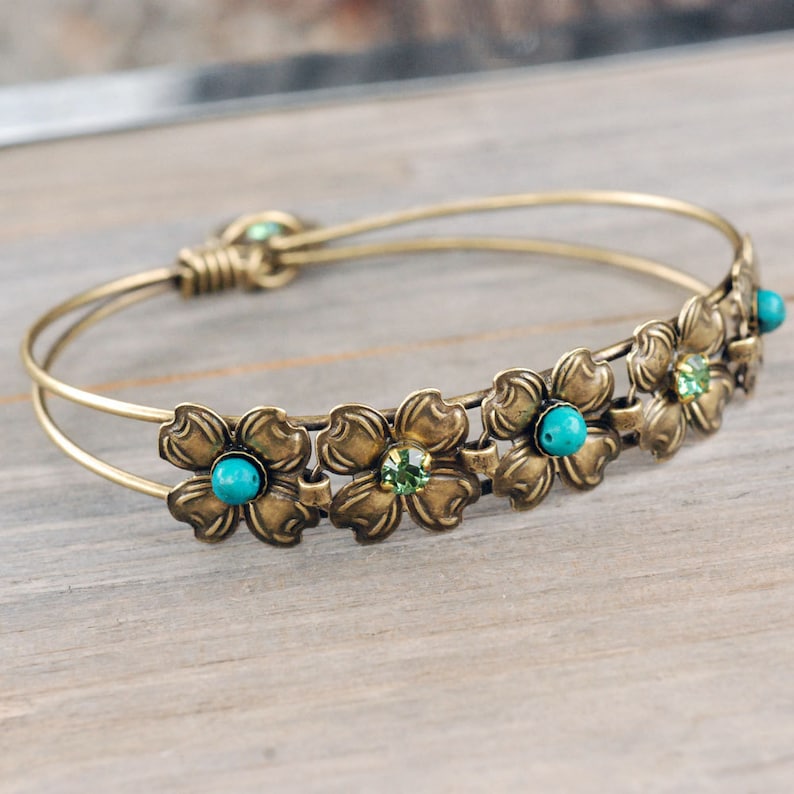 May include: A gold-toned bangle bracelet with a double wire design. The bracelet is adorned with five flower-shaped charms, each with a turquoise and green gemstone in the center.