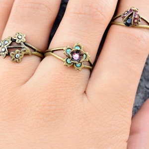May include: Three rings with floral and ladybug designs. The rings are made of gold-toned metal and feature colorful rhinestones.
