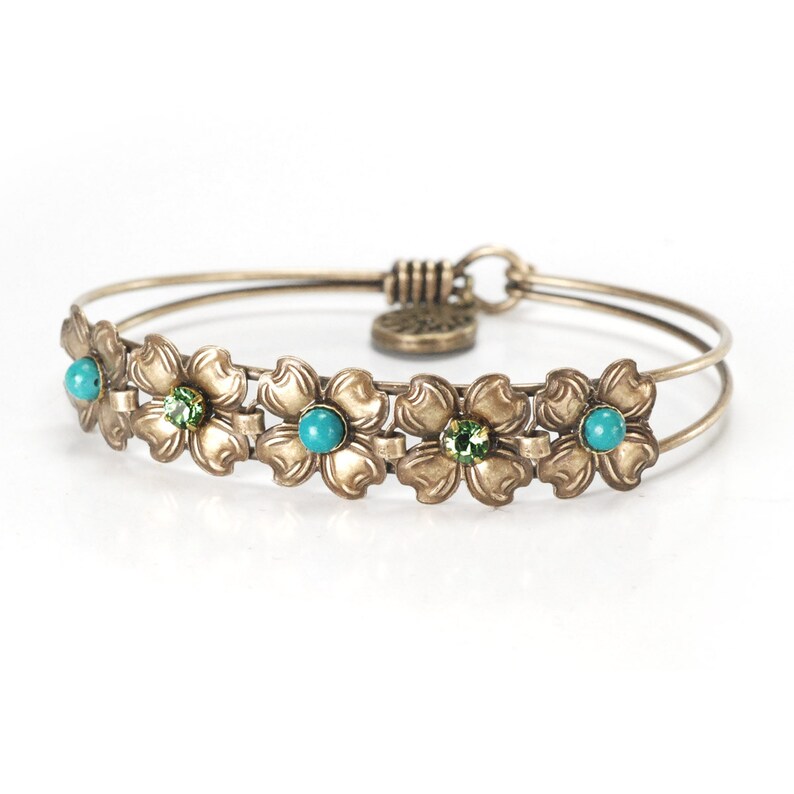 May include: A gold-toned bangle bracelet with a floral design. The bracelet features five flowers with turquoise and green gemstones.