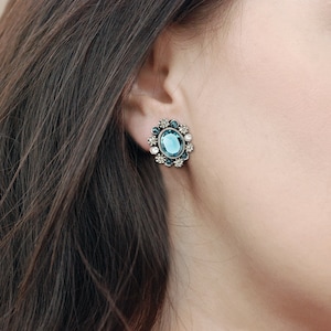 Puede incluir: Un par de pendientes azules y plateados con una gran piedra ovalada azul rodeada de piedras azules y blancas m&aacute;s peque&ntilde;as.
