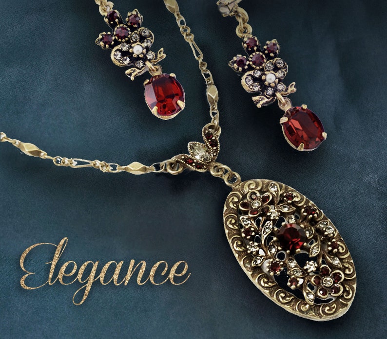 May include: A gold necklace with a red and white floral pendant and matching earrings. The necklace features a delicate chain and a large oval pendant with intricate details. The earrings are small and feature a cluster of red and white stones.