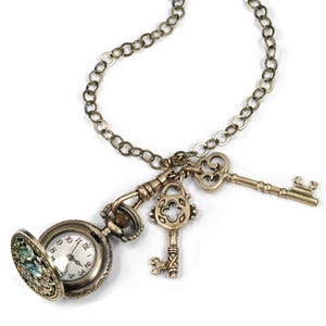 May include: A gold chain necklace with a pocket watch, a key, and a heart-shaped key charm. The pocket watch has a white face with black numbers and hands.
