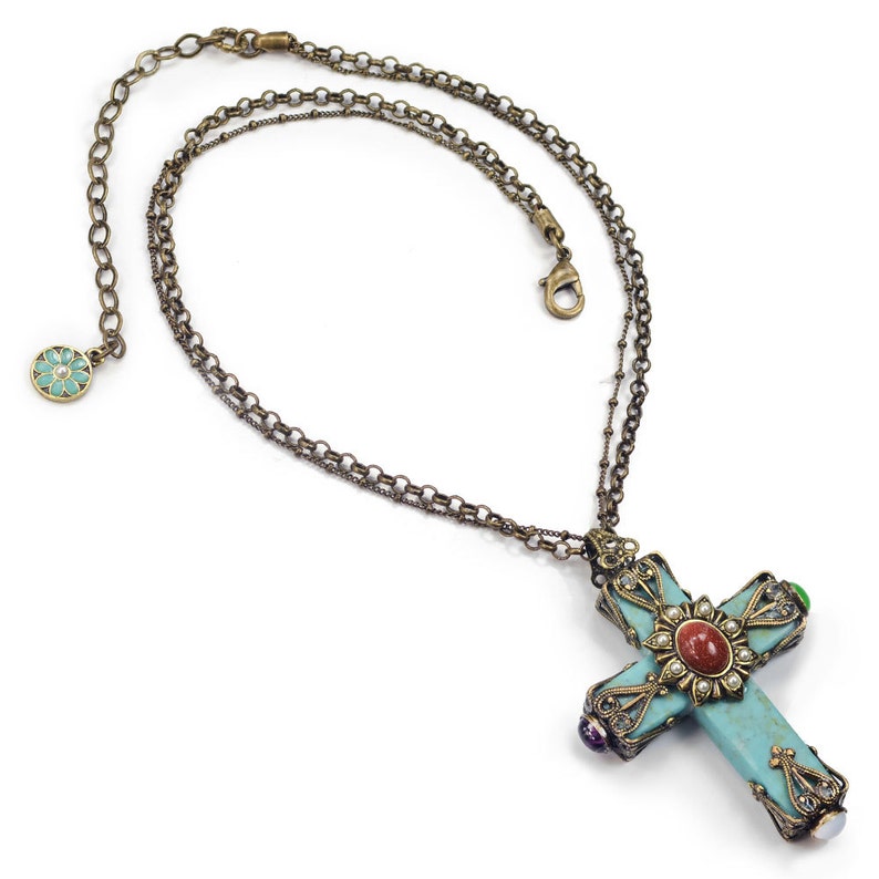 May include: A turquoise cross pendant necklace with a double chain. The cross is decorated with colorful gemstones and a red stone in the center.