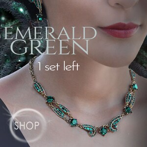 May include: A gold necklace with emerald green stones in a leaf design. The necklace is on a model's neck. The text "EMERALD GREEN" and "1 set left" is on the image. There is a button that says "SHOP".
