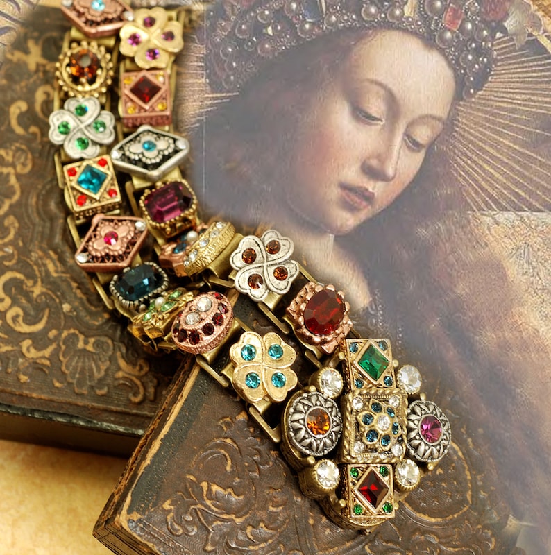 May include: A gold-toned bracelet with a multi-colored design featuring various gemstones and clover charms. The bracelet is on a brown surface with a painting of a woman in the background.