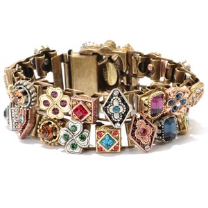 May include: A gold-tone bracelet with a chain link design and multiple colorful, jeweled charms. The charms include squares, diamonds, and four-leaf clovers.