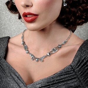 May include: A silver necklace with a delicate design featuring small, clear stones. The necklace has a pendant with a teardrop shape and a cluster of smaller stones.