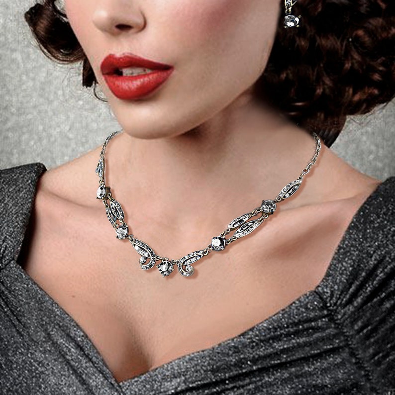 May include: A silver necklace with a delicate design featuring small, clear stones. The necklace has a pendant with a teardrop shape and a cluster of smaller stones.